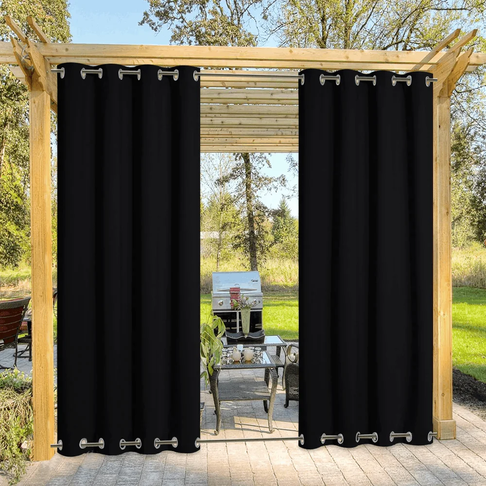 Heavy black outdoor privacy curtains with silver grommets at the top and bottom, installed on a wooden pergola over a stone patio.