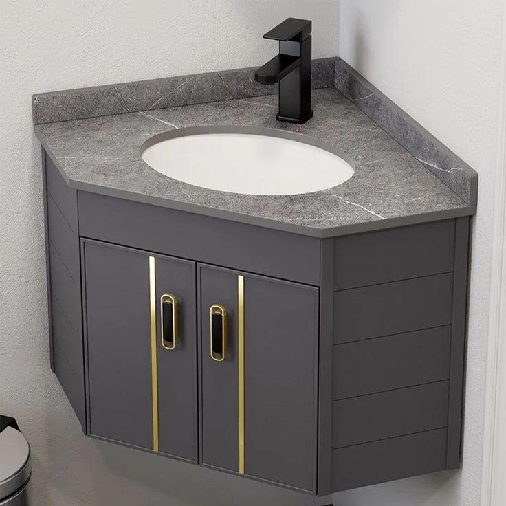 Modern wall-mounted corner bathroom vanity in charcoal grey featuring a grey marble-textured countertop, an oval undermount sink, a matte black faucet, and cabinet doors accented with vertical gold trim and handles.