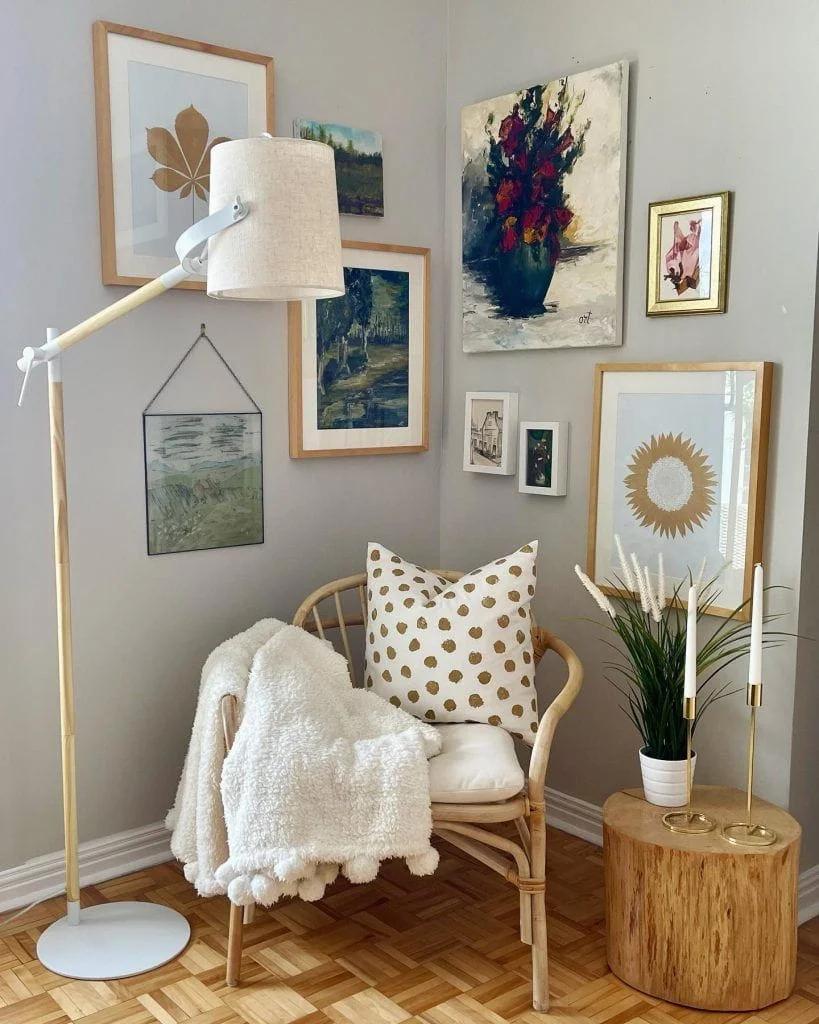 How to Turn an Empty Corner into a Cozy Reading Nook A cozy reading nook created in a room corner with a rattan accent chair, a textured gallery wall of nature art, a tall wooden floor lamp, and a natural log side table.