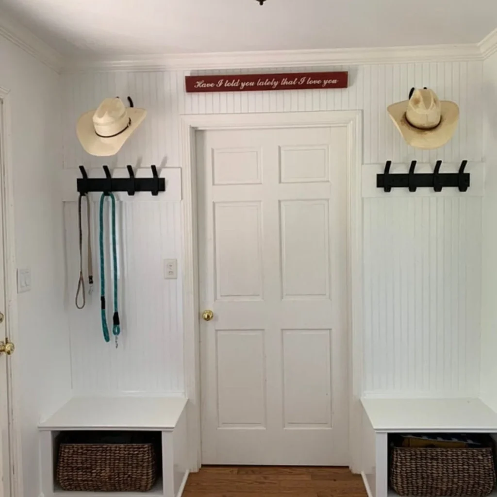 Entryway Coat Rack and Storage Benches Symmetrical white entryway mudroom setup with black coat hooks, cowboy hats, and wicker storage baskets.