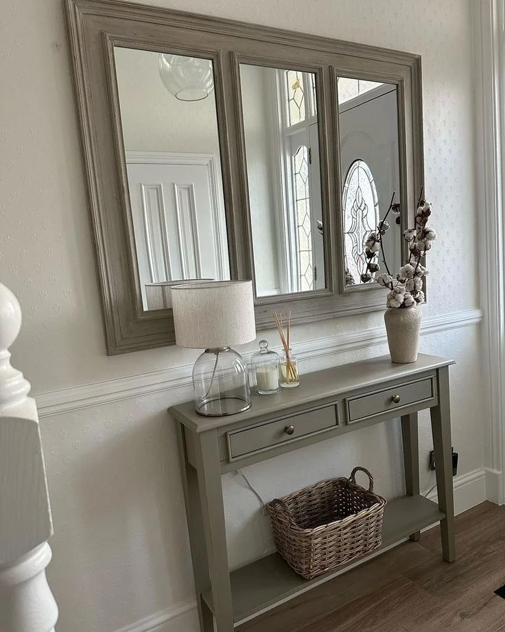 Minimalist Hallway Console Table with Large Paneled Mirror Minimalist entryway decor featuring a grey narrow console table with drawers, a wicker storage basket underneath, and a large horizontal triptych wall mirror in a farmhouse or Japandi style hallway.
