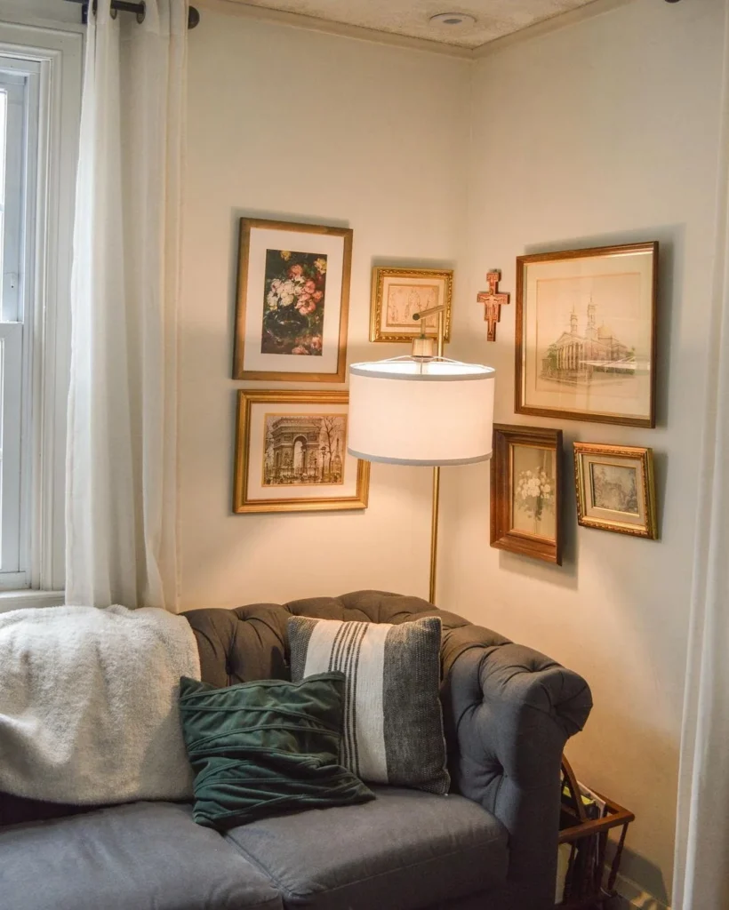 vintage living room corner decor with gallery wall and floor lamp Cozy living room corner featuring a dark grey tufted sofa with green and striped throw pillows, styled with a warm brass floor lamp and an eclectic gallery wall of vintage framed art prints.