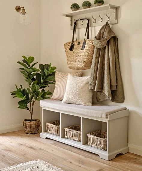 small hallway storage bench ideas A cozy entryway corner featuring a light grey wooden storage bench with a padded seat cushion, three wicker baskets underneath, decorative throw pillows, and a matching wall-mounted coat rack.