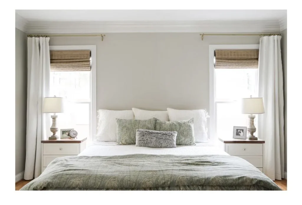 Symmetrical modern bedroom setup featuring a bed flanked by two windows, each fitted with woven bamboo woven shades and framed by white curtain drapes on brass rods.