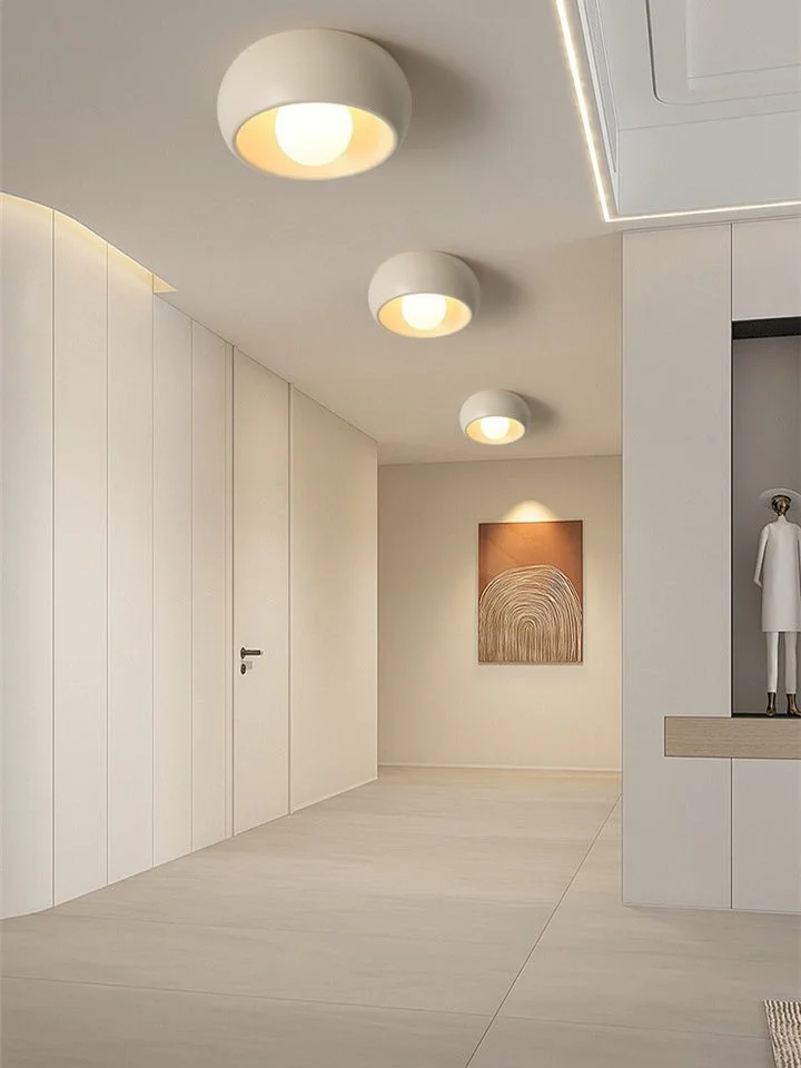 Row of cream-colored dome flush mount lights illuminating a minimalist white entryway corridor with warm lighting.