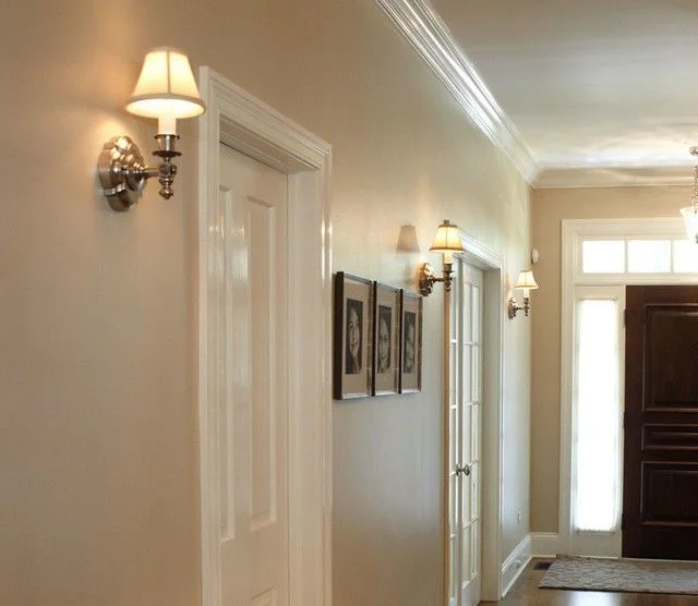 Classic chrome wall sconces with mini lampshades illuminating a warm, neutral-toned home hallway next to white paneled doors.