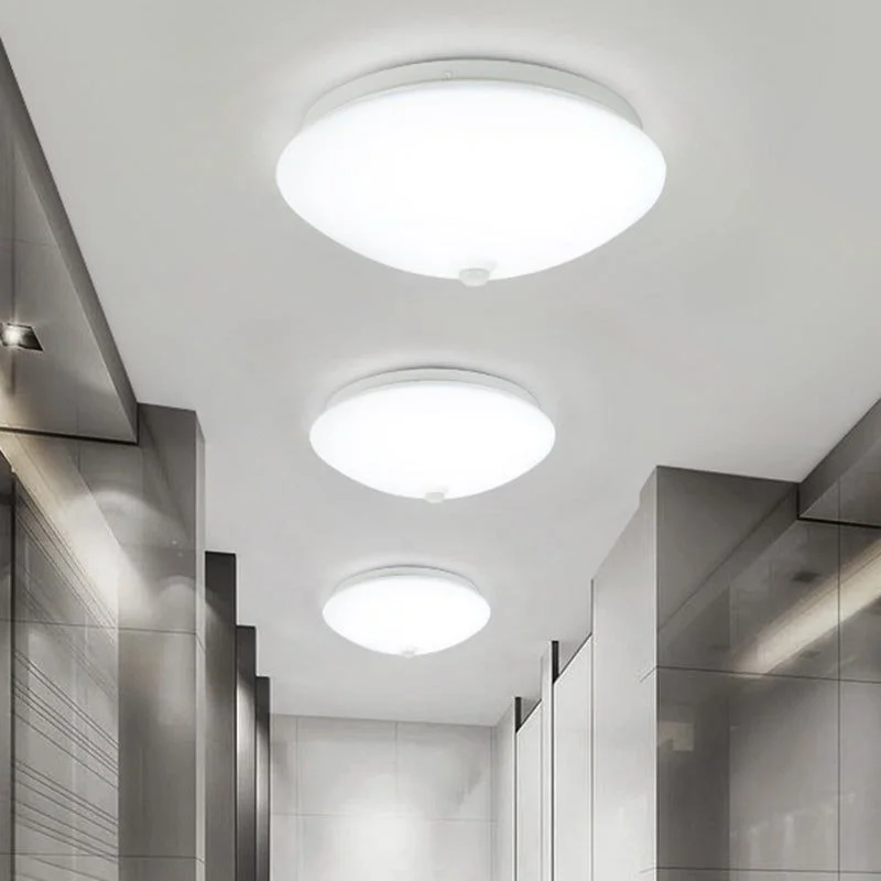 Three round, white minimalist motion sensor ceiling  lights illuminating a modern hallway with grey tiled walls.