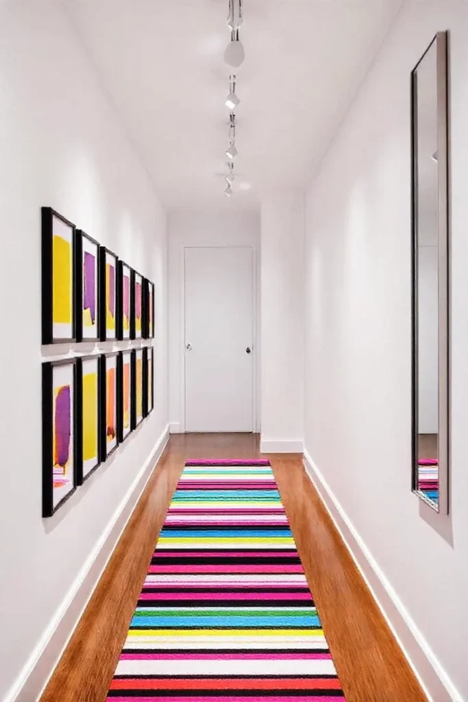 A narrow white hallway featuring a bright, multi-colored striped runner rug with horizontal lines of pink, blue, yellow, green, and black on a medium-toned hardwood floor.