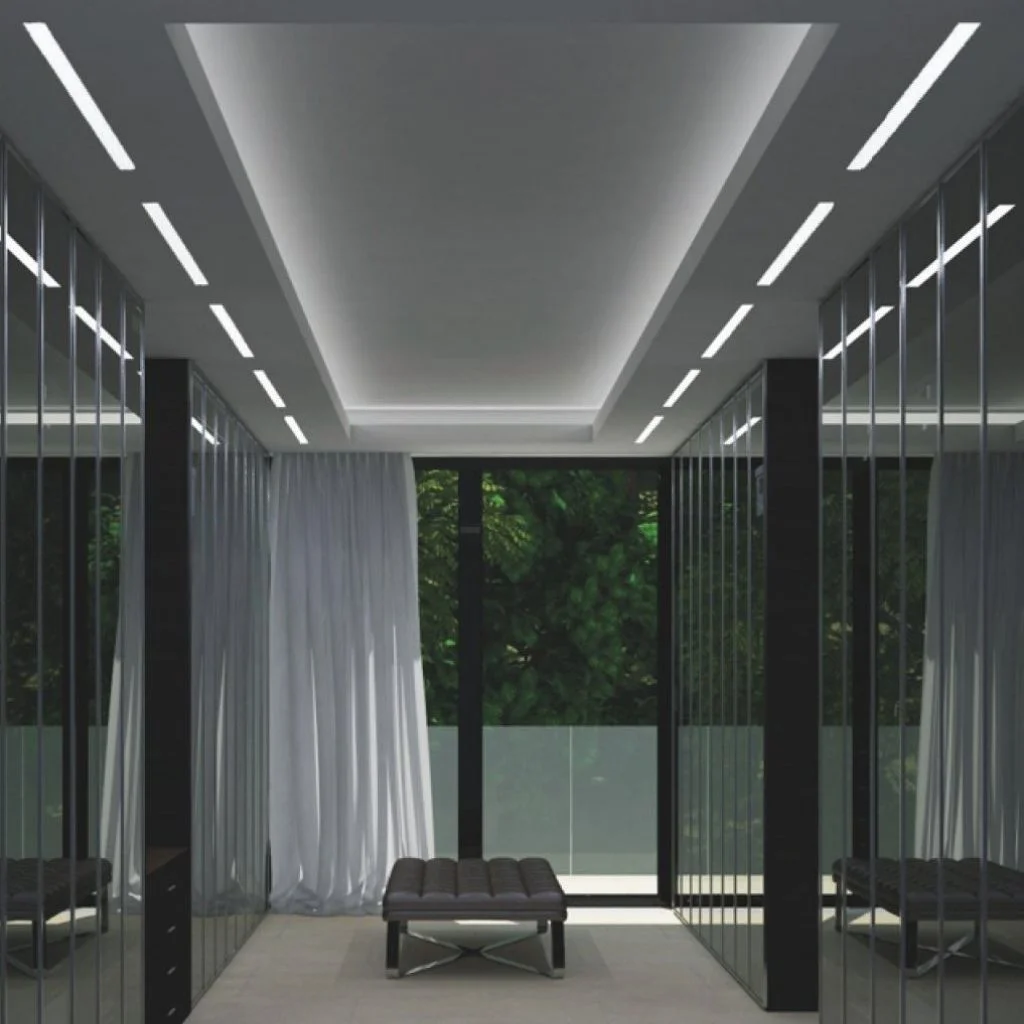 A minimalist modern hallway featuring mirrored wall panels on both sides, a tray ceiling with recessed linear LED lighting, a dark tufted bench in the center, and a large window at the end showcasing green foliage.