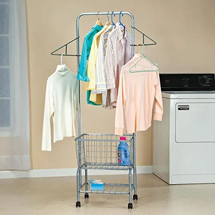 Freestanding silver metal laundry cart on wheels featuring a top garment hanging bar with side wing arms holding shirts on hangers, a lower wire storage basket containing detergent, and a bottom wire shelf next to a white washing machine.