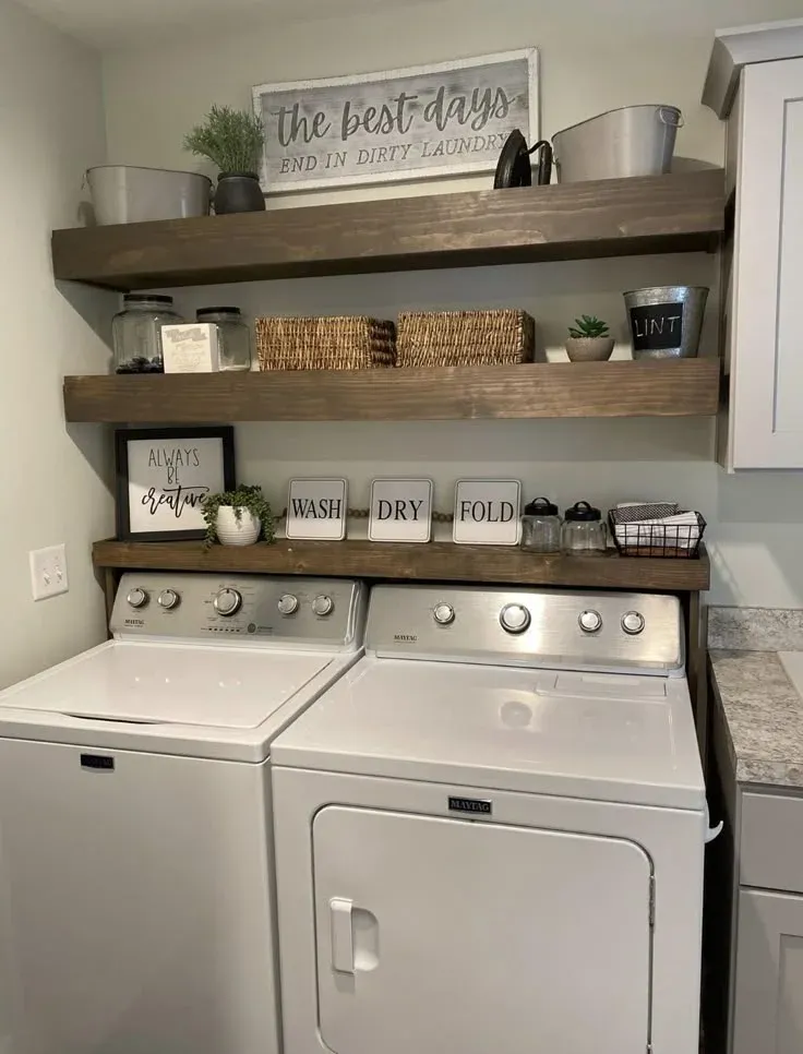 Warm, rustic laundry room organization featuring dark walnut floating shelves, cute quote wall art, galvanized metal accents, glass storage jars, and woven baskets over a clean Maytag washer and dryer unit.