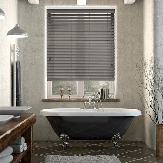 Charcoal gray slatted horizontal window blinds mounted above a black vintage bathtub with silver fixtures.
