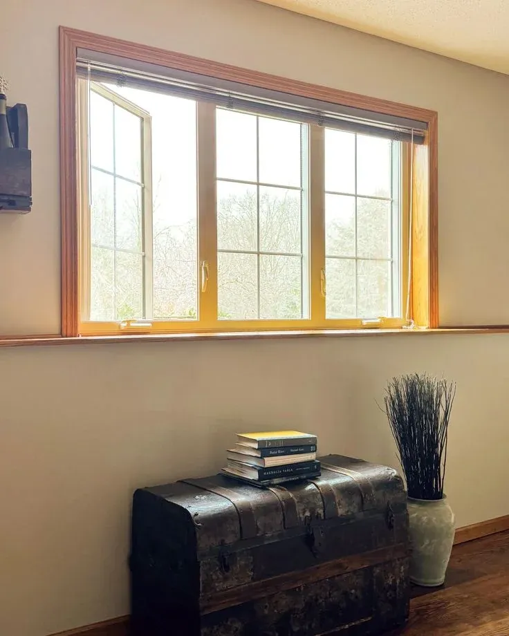Wood-framed multi-pane casement window partially open above an antique chest and decorative tall vase.
