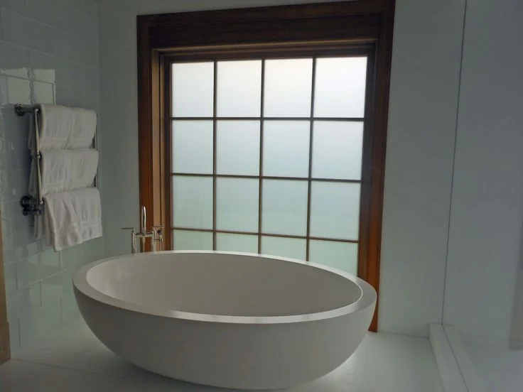 Modern bathroom featuring an oval soaking tub and a wood-framed window with frosted privacy glass panes.