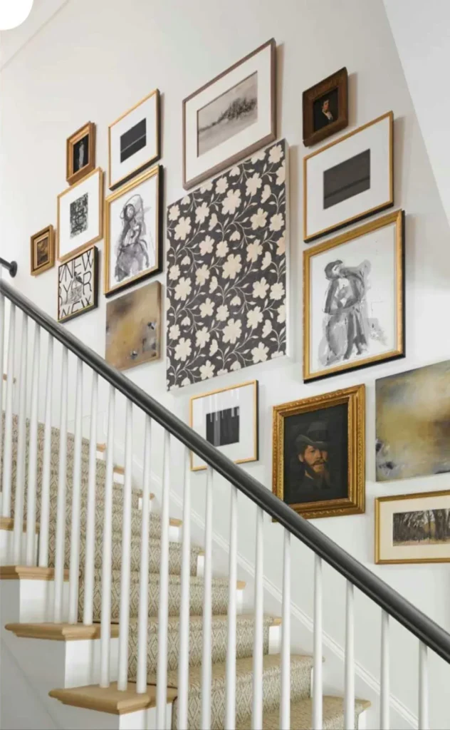 Traditional staircase gallery wall featuring a mix of gold and wooden picture frames, vintage portraits, abstract art, and a patterned fabric canvas along a white painted wall.