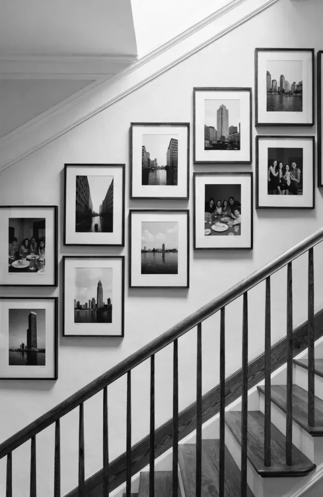 Minimalist staircase gallery wall featuring black-and-white city skylines and family portraits in matching thin black frames along a white wall.