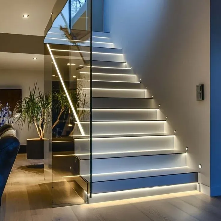 Contemporary interior staircase design with cool white LED step lighting, glass balustrade, and minimalist side wall lights.
