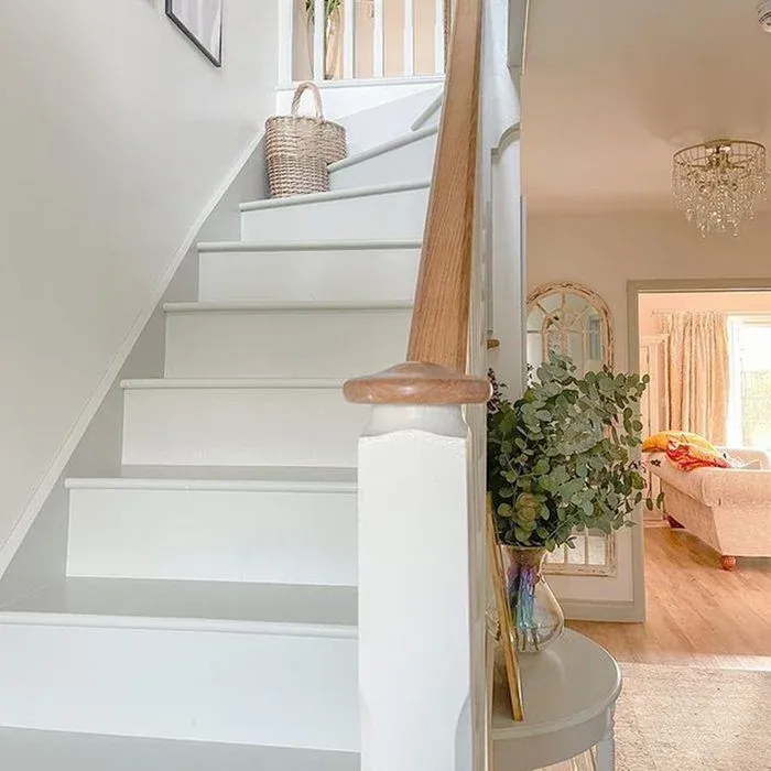 Bright modern staircase featuring freshly painted white steps and risers paired with a smooth natural oak handrail, with a small woven basket near the top landing and a glass vase filled with green eucalyptus leaves on an entryway table nearby.