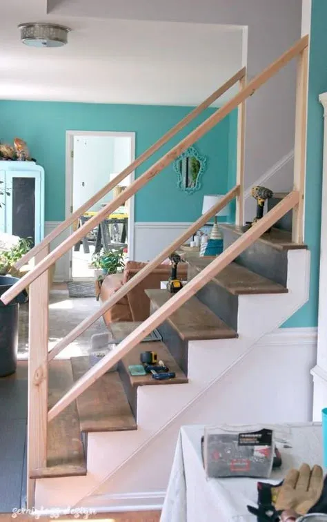 Work-in-progress DIY staircase makeover showing raw light wood framing lumber being installed for a new handrail and balusters, with power tools sitting on dark wooden treads against bright teal accent walls.