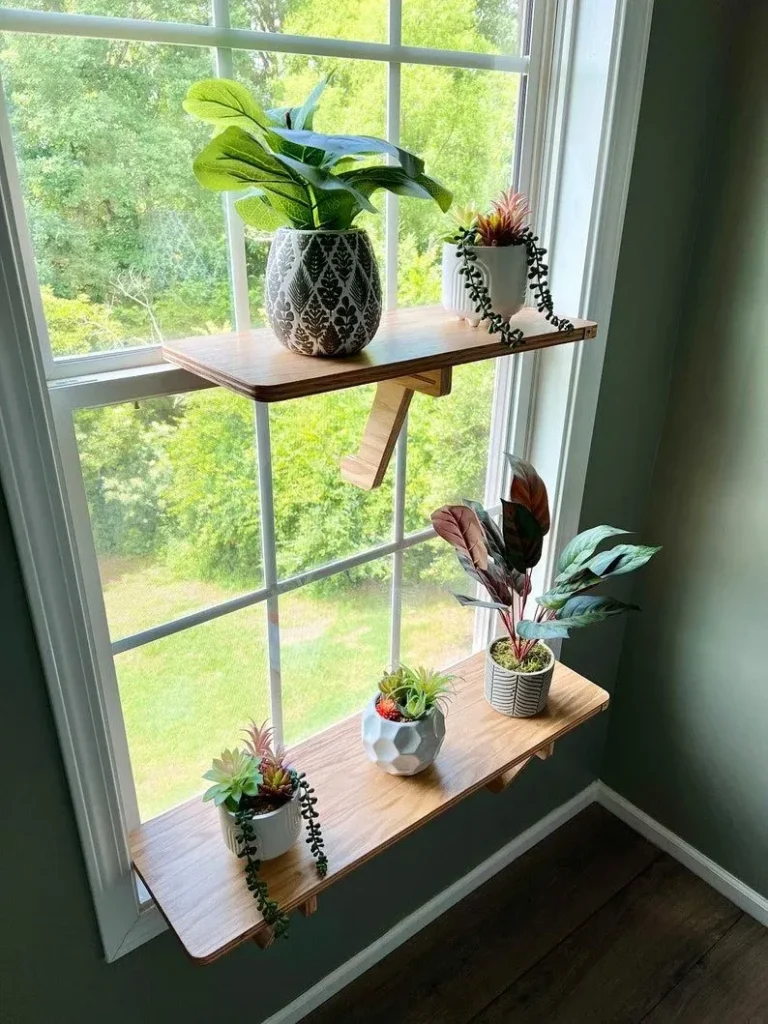 Two wooden window sill shelves supported by brackets, mounted in front of a white frame window to display potted houseplants and succulents.