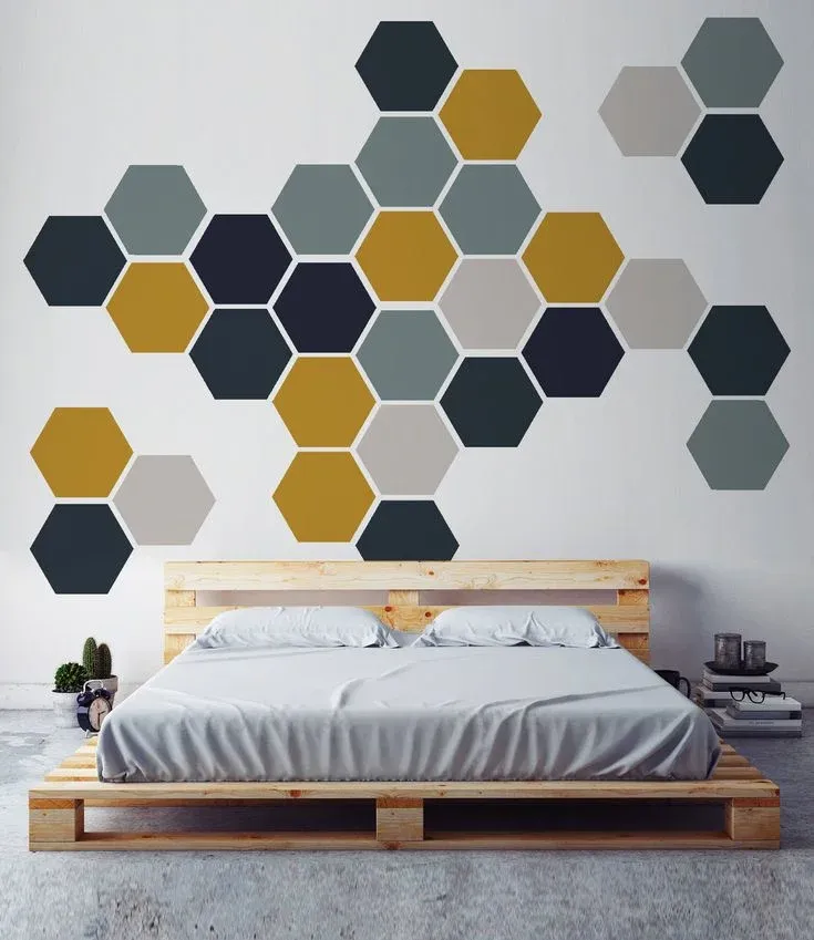 Modern bedroom featuring a wooden pallet bed frame and an accent wall decorated with removable honeycomb hexagon wall decals in dark blue, mustard yellow, and grey.