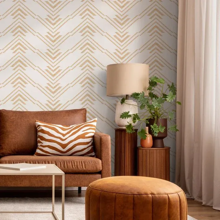 Neutral warm living room featuring removable geometric wallpaper with gold chevron chevron patterns behind a cognac leather sofa and brown leather ottoman.